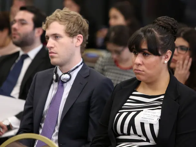 In this image we can see some people sitting on chairs. One person is holding a paper in his hand....