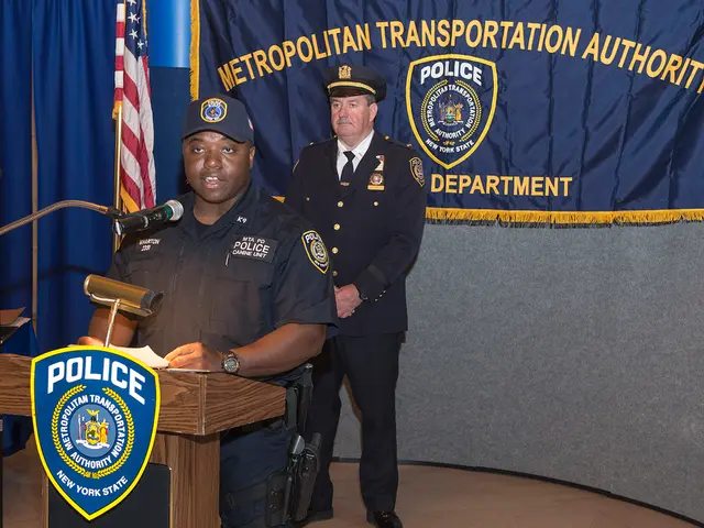 In this image we can see two police officers, one of them is holding some papers, and talking in...