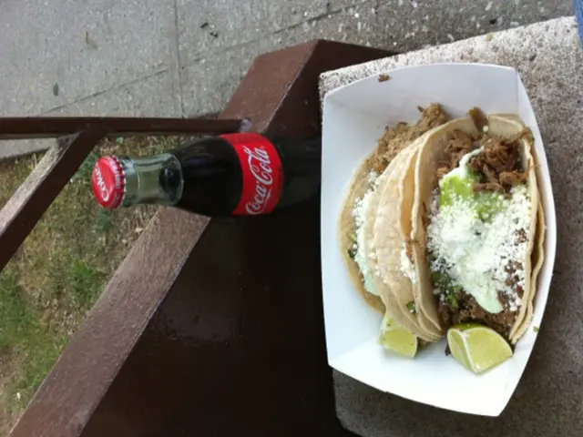 There is a snack item kept on a bench and behind the snack there is a cold drink bottle, behind the...