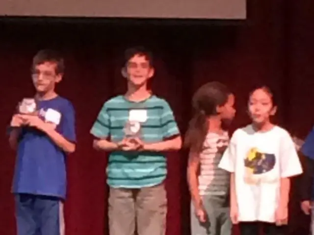 In the middle a boy is standing, he wore shirt, trouser. On the right side 2 girls are standing.