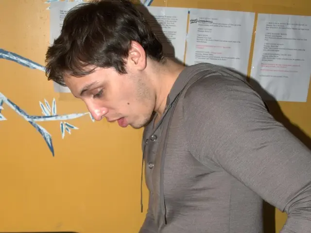 In this image the man is standing and holding a glass bottle in his hands. On the left side of the...