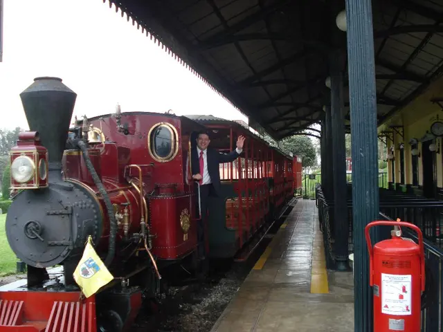 In this picture we can see the red color old train and a man wearing black color suit, standing at...